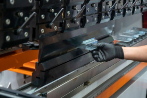 A person wearing a black glove operates a metal presswork machine