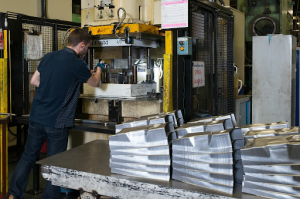A factory worker operates a metal presswork machine surrounded by tools