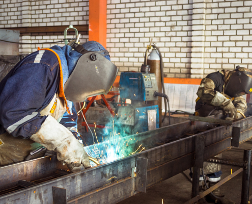 A factory worker welding metal components, surrounded by industrial equipment and bright sparks