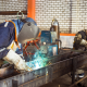 A factory worker welding metal components, surrounded by industrial equipment and bright sparks