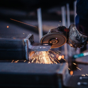 A welder uses a grinding tool on metal, producing flying sparks in a workshop setting.