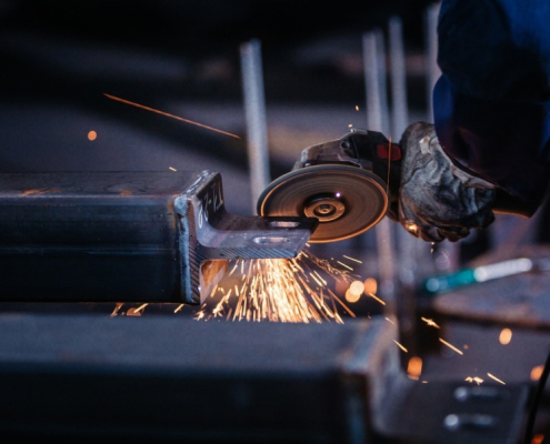 A welder uses a grinding tool on metal, producing flying sparks in a workshop setting.