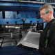 A man with glasses is holding a sheet of metal, indicating his involvement in a project or craft activity