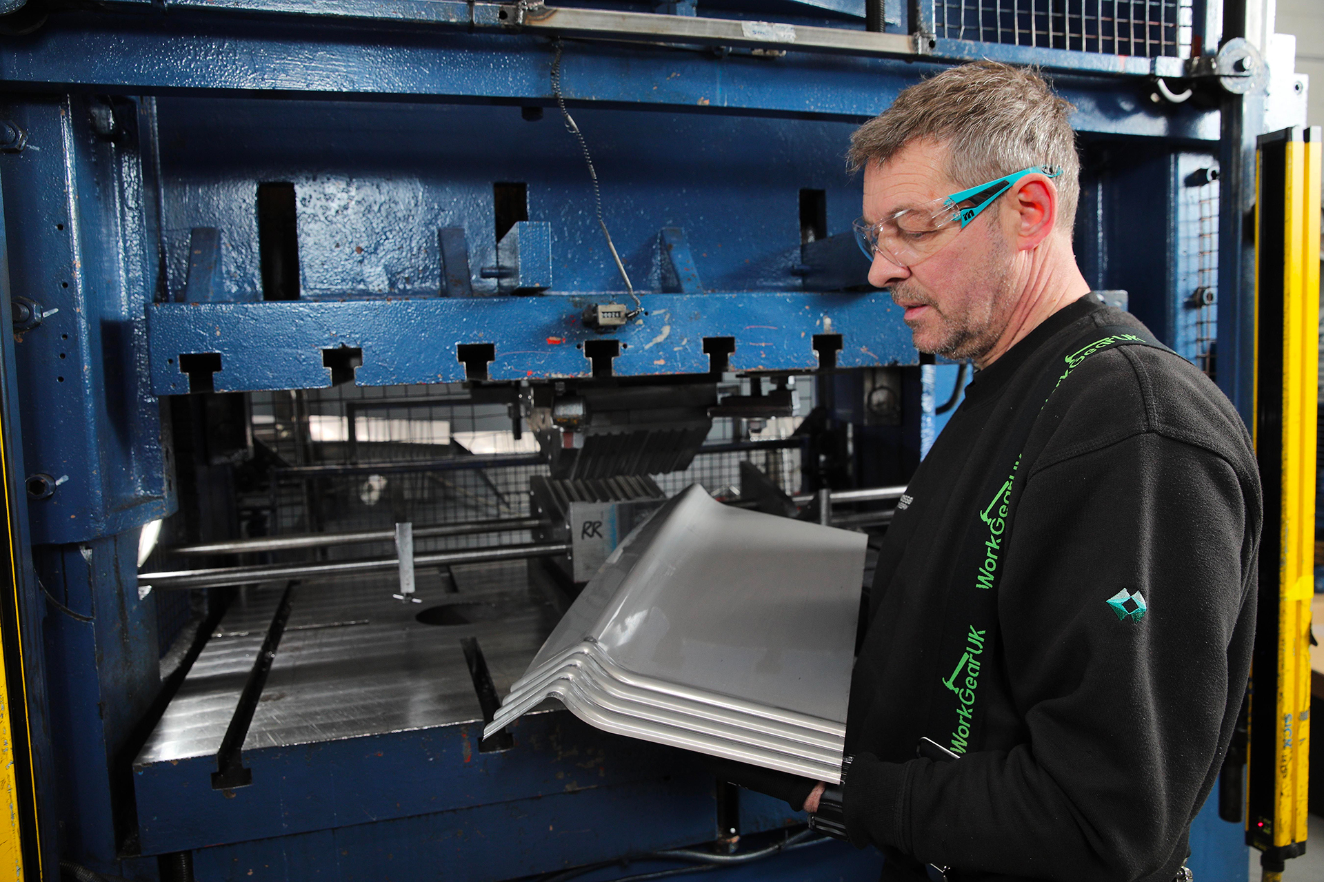 A man with glasses is holding a sheet of metal, indicating his involvement in a project or craft activity