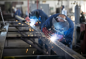 Welder working in a factory, joining steel parts with a welding machine