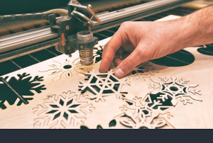 A person operates a laser cutter to create an intricate snowflake design from a sheet of material