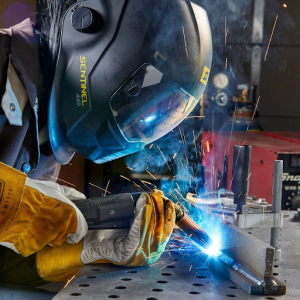 A person wearing a welding helmet is focused on welding metal pieces together