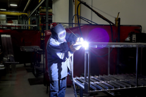 A man using a welding torch to weld metal in a factory setting. Sparks fly as he focuses on his work. 