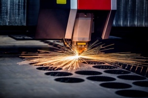 A laser cutting machine operates, precisely cutting through a sheet of metal in a workshop setting. 