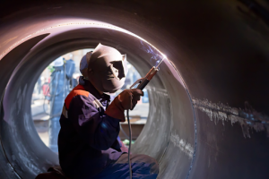 A helmeted man is welding a pipe