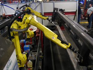 A yellow robot is assembling components on a metal frame in a workshop setting