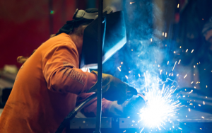 A man engaged in metal fabrication, welding with flying sparks in a bustling industrial environment. 