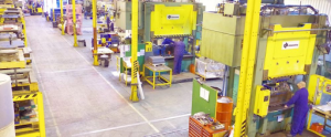 A factory interior showing workers operating various machines in a busy industrial environment. 