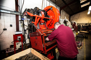 A man operates a machine in a workshop, focused on his task amidst tools and equipment. 