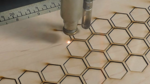 A laser cutting a precise hexagon pattern into a wooden surface. 