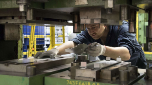 A worker in a factory adjusts metal presswork machinery,