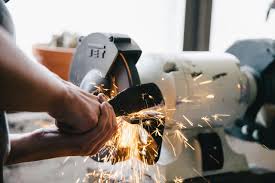 A man operates a metal grinder, creating sparks as he shapes the metal piece. 