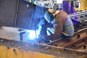 A man welding a metal structure inside a factory, wearing protective gear