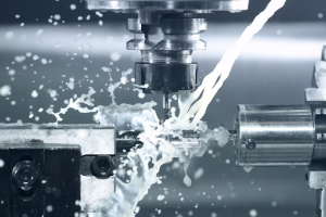 A machine cuts through metal, creating splashes of water as it works on the material. 