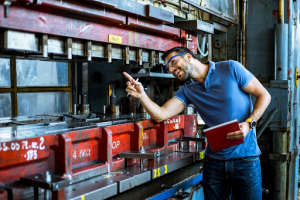 A man stands in front of a large machine, observing its operation with a focused expression